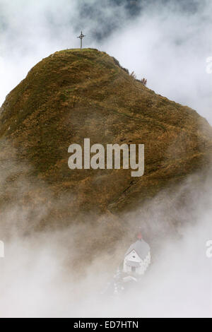 In piedi di una croce e una piccola cappella bianca su una montagna, travolto in una nuvola. Un lone sentiero conduce dalla cappella alla croce. Lo Foto Stock