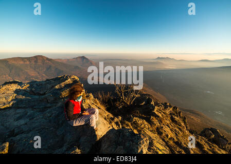 Escursionista femmina di raggiungere il suo obiettivo alla cima della montagna e guardando il maestoso panorama italiano della Alpi occidentali con la nebbia Foto Stock