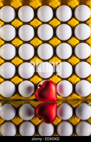 Palline da golf nel foglio di carta cartone per le uova e il simbolo di amore su una scrivania in vetro Foto Stock