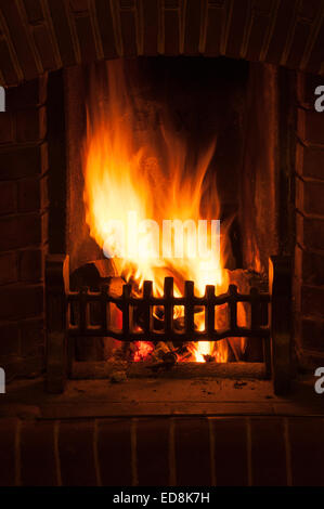 Bagliore calorosamente di un tradizionale scena invernale come un fuoco aperto in una casa irradia luce incandescente come brace di legno e carbone masterizzare hot Foto Stock