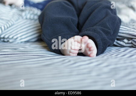 Piedi del bambino su un letto con lenzuola a strisce Foto Stock