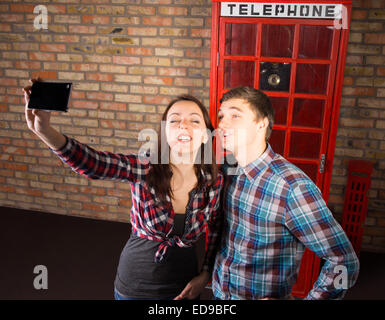 Giovani turisti in posa davanti un iconico red britannico phone booth prendendo un selfie sul proprio telefono cellulare Foto Stock