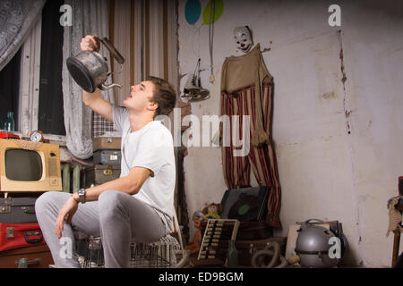 Giovane uomo in abito Casual bere qualcosa dal vecchio bollitore mentre è seduto sulla gabbia. Foto Stock