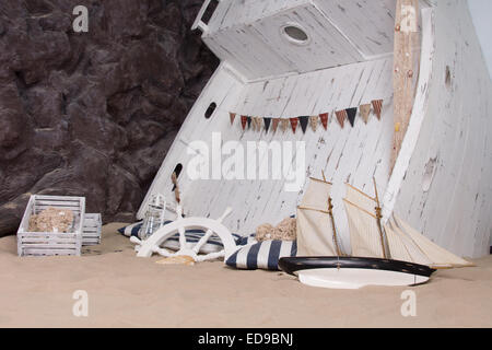 Marine o a tema nautico ancora vita raffigurante un relitto di nave con una barca di legno sconvolto nella sabbia con una ruota di navi, lanterna, Foto Stock