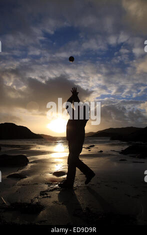 Knockvologan, Isle of Mull, Scozia. Il 2 gennaio, 2015. Venti estremi del 2 gennaio 2015 morire in giù dando un breve restbite ad un bellissimo tramonto sulla spiaggia Knockvologan sull'Isle of Mull in Scozia Ebridi Interne. Un uomo prende vantaggio del cambiamento di clima e prende un po' di aria fresca e gettando in una sfera di circa sulla spiaggia. Credito: PictureScotland/Alamy Live News Foto Stock