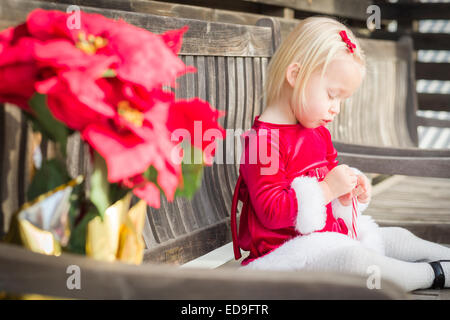 Adorabili poco ragazza seduta su una panchina con la sua Candy Cane all'esterno. Foto Stock