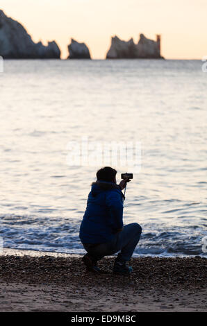 Un uomo con un 'selfie stick' ad Alum Bay sull'Isola di Wight con gli aghi nella distanza Foto Stock