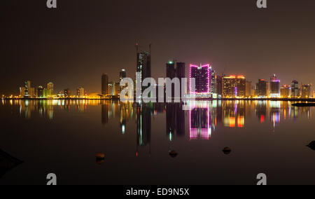 Notte moderno skyline della città con brillanti luci al neon e riflessi nell'acqua. Manama, Bahrein, Medio Oriente Foto Stock