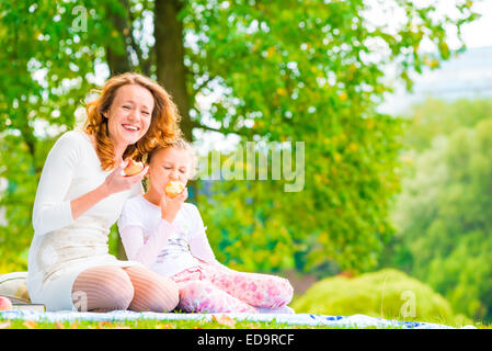 Giovane madre e figlia di mangiare le mele nel parco Foto Stock