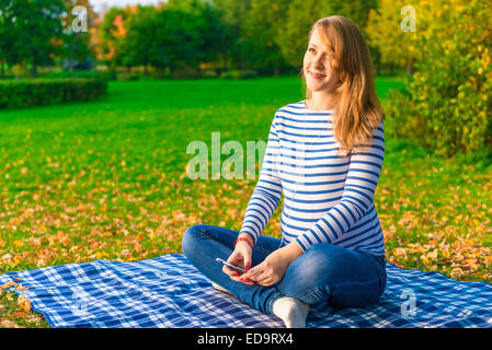 Donna incinta ascoltare musica classica in autunno park Foto Stock