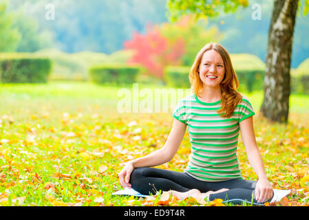 Resto in autunno park. donna le pratiche yoga sulla natura Foto Stock