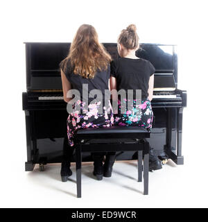 Due ragazze adolescenti e nero pianoforte verticale in studio contro uno sfondo bianco Foto Stock