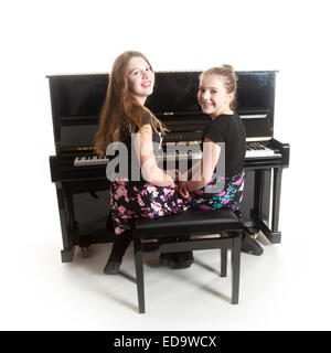 Due ragazze adolescenti e nero pianoforte verticale in studio contro uno sfondo bianco Foto Stock