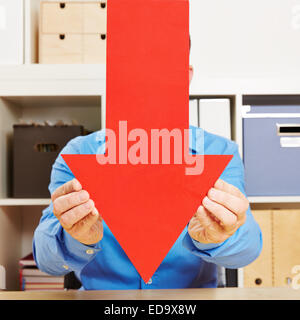 Business man holding grande freccia rossa verso il basso in ufficio Foto Stock