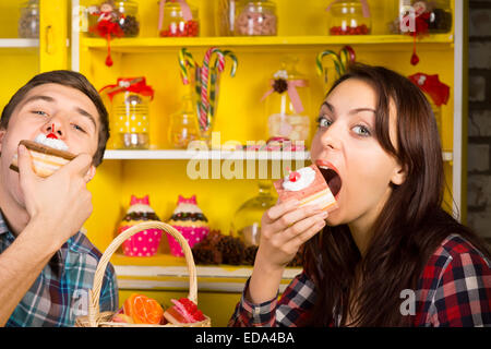 Coppia giovane facendo mangiare una torta pongono presso il Cafe mentre guardando la telecamera. Catturato con la caramella giare il display sul retro. Foto Stock