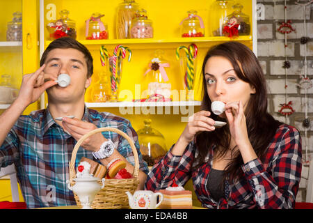 Chiudere fino bianco giovane coppia in abiti casual facendo sorseggiando un drink pongono da piccole tazze bianche mentre guardando la telecamera. Capt Foto Stock