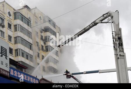 (150104) -- HARBIN, gen. 4, 2015 (Xinhua) -- Vigili del Fuoco spruzzare acqua ad un magazzino bruciato a Beifangnanxun mercato della ceramica nel distretto Daowai, Harbin, capitale del nord-est della Cina di Provincia di Heilongjiang, gen. 4, 2014. Il magazzino blaze in Harbin City che ha ucciso 5 i vigili del fuoco non è ancora stato completamente spento, i vigili del fuoco locali detto Domenica. Al 10:40 a.m. Domenica, un edificio residenziale accanto al magazzino era ancora fumante. Soccorritori ha detto che la fonte del fuoco è stata difficile da determinare a causa della costruzione di una struttura complicata, e l'edificio è a rischio di c Foto Stock