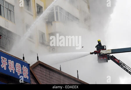 (150104) -- HARBIN, gen. 4, 2015 (Xinhua) -- un vigile del fuoco spruzza acqua a un magazzino bruciato a Beifangnanxun mercato della ceramica nel distretto Daowai, Harbin, capitale del nord-est della Cina di Provincia di Heilongjiang, gen. 4, 2014. Il magazzino blaze in Harbin City che ha ucciso 5 i vigili del fuoco non è ancora stato completamente spento, i vigili del fuoco locali detto Domenica. Al 10:40 a.m. Domenica, un edificio residenziale accanto al magazzino era ancora fumante. Soccorritori ha detto che la fonte del fuoco è stata difficile da determinare a causa della costruzione di una struttura complicata, e l'edificio è a rischio di Foto Stock