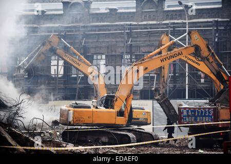 (150104) -- HARBIN, gen. 4, 2015 (Xinhua) -- macchine pesanti eliminare i detriti di un magazzino bruciato a Beifangnanxun mercato della ceramica nel distretto Daowai, Harbin, capitale del nord-est della Cina di Provincia di Heilongjiang, gen. 4, 2014. Il magazzino blaze in Harbin City che ha ucciso 5 i vigili del fuoco non è ancora stato completamente spento, i vigili del fuoco locali detto Domenica. Al 10:40 a.m. Domenica, un edificio residenziale accanto al magazzino era ancora fumante. Soccorritori ha detto che la fonte del fuoco è stata difficile da determinare a causa della costruzione di una struttura complicata, e l'edificio è a r Foto Stock