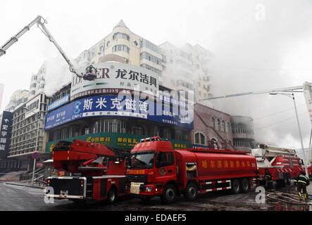 (150104) -- HARBIN, gen. 4, 2015 (Xinhua) -- Vigili del Fuoco tentare di abbattere i cartelloni durante un incendio estinzione di missione su un magazzino bruciato a Beifangnanxun mercato della ceramica nel distretto Daowai, Harbin, capitale del nord-est della Cina di Provincia di Heilongjiang, gen. 4, 2014. Il magazzino blaze in Harbin City che ha ucciso 5 i vigili del fuoco non è ancora stato completamente spento, i vigili del fuoco locali detto Domenica. Al 10:40 a.m. Domenica, un edificio residenziale accanto al magazzino era ancora fumante. Soccorritori ha detto che la fonte del fuoco è stata difficile da determinare a causa della costruzione di' Foto Stock