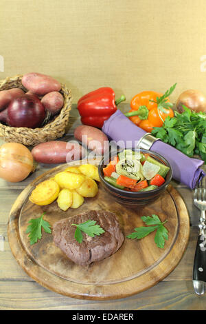 Arrosto bistecche di carne di struzzo con patate al forno e le verdure su una tavola di legno Foto Stock