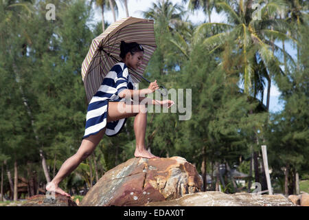 Donna in abito a righe con ombrellone a piedi di rocce Foto Stock