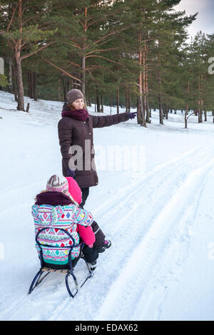 Famiglia caucasica sulle passeggiate d'inverno. Madre tira la slitta con le sue due figlie Foto Stock