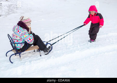 Little Baby girl in rosa tirando una slitta sulla strada innevata Foto Stock