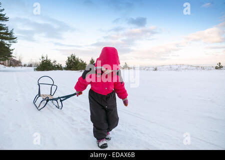 Little Baby girl in rosa tirando una slitta sulla strada innevata Foto Stock