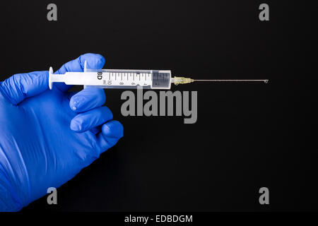 Una mano con un blu guanto medicale è in possesso di una siringa Foto Stock