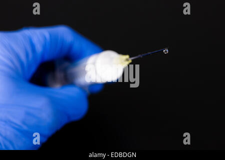 Una mano con un blu guanto medicale è in possesso di una siringa con un ago ipodermico e una goccia di medicina Foto Stock