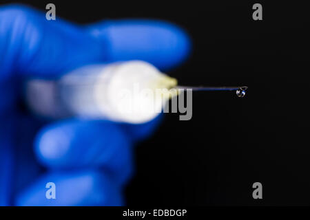 Una mano con un blu guanto medicale è in possesso di una siringa con un ago ipodermico e una goccia di medicina Foto Stock