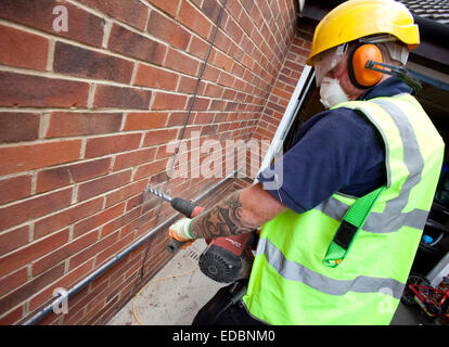 Immagine illustrativa della parete di cavità di isolamento. Un lavoratore di totale isolamento trapani soluzioni di un foro per consentire l'isolamento di rockwool per essere inserita. Foto Stock