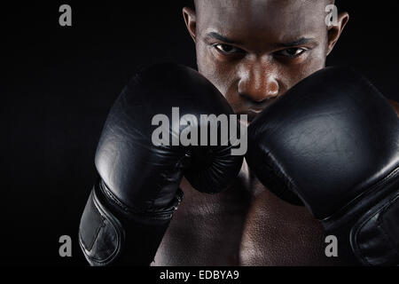 Ritratto di un giovane maschio boxer in un atteggiamento di combattimento su sfondo nero. Giovane uomo facendo esercizio di inscatolamento. Foto Stock