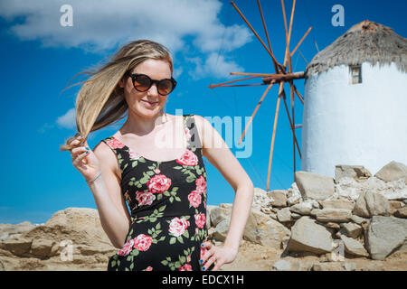 Giovane ragazza bionda con occhiali da sole al mulino a vento a Mykonos Foto Stock