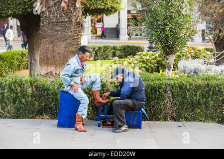 Lo stile di vita locale: uomo peruviano Vestito in blu denim avente il suo smart stivali marrone irraggiata da un vecchio uomo in Plaza de Armas, downtown Arequipa, Perù Foto Stock