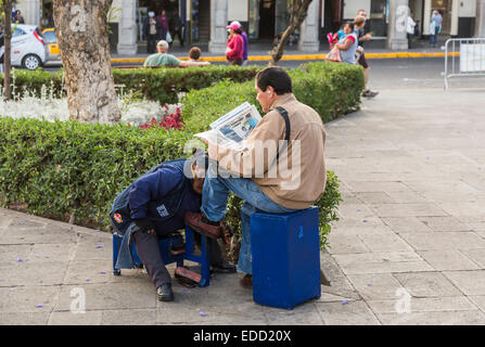 Lo stile di vita peruviano: locali Peruviani uomo che legge il giornale mentre avente le sue scarpe lucidate in Plaza de Armas, downtown Arequipa, Perù Foto Stock