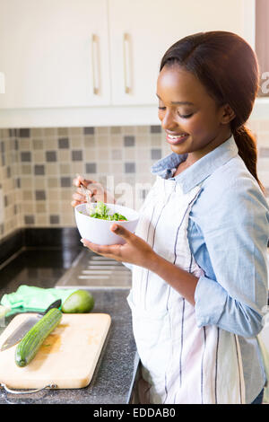 Felice casalinga africana di mangiare insalata verde in cucina Foto Stock