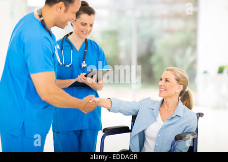 Gentile di mezza età medico lo handshaking con paziente su sedia a rotelle Foto Stock