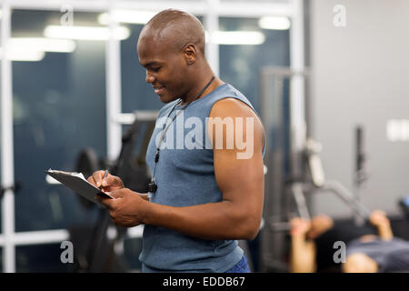 Vista laterale del maschio africano istruttore di palestra iscritto negli appunti Foto Stock