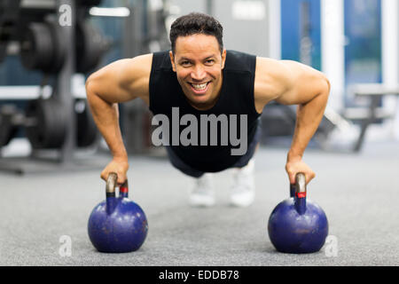Uomo sano facendo esercizio di spinta in su con bollitore campana in palestra Foto Stock