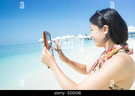 Maldive atollo di Ari, giovane donna prendendo fotografia con la sua mini tablet Foto Stock