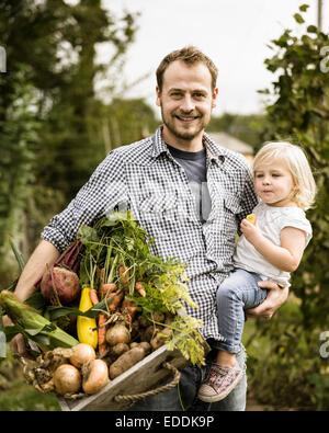 Uomo in piedi nel suo riparto con sua figlia, sorridente, tenendo una scatola piena di appena raccolto verdure. Foto Stock