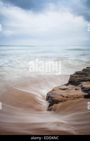 Le onde impetuose su rocce nere. Northumberland. In Inghilterra. Regno Unito. Foto Stock