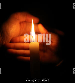 Mano protegge la fiamma di una candela la masterizzazione su uno sfondo scuro Foto Stock