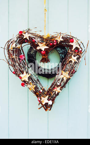 A forma di cuore ad ghirlanda fatta con ramoscelli, stelle e frutta secca su luce porta blu Foto Stock