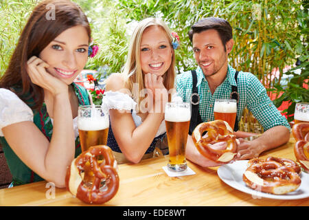 Happy amici seduti nel giardino della birra in Baviera con pretzel Foto Stock