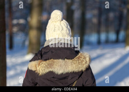 Retro di una giovane donna nel pensare abbigliamento invernale come si guarda verso una foresta innevata. Foto Stock