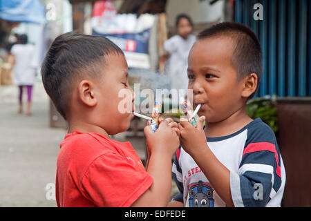 Bambini indonesiano di essere insegnato come fumo da parte essendo consentito a soffio di distanza su fatti in casa a base di tubi, chiamato Popeye Lauts, Indonesia Foto Stock