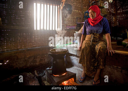 Anziani indonesiano, donna la cottura del riso nella tradizionale casa di bambù, Cianjur Regency, West Java, Indonesia Foto Stock